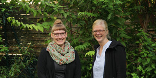 Portraitaufnahme: Kim Lipinski (links) und Sabine Stroth (rechts) vor grüner Hecke