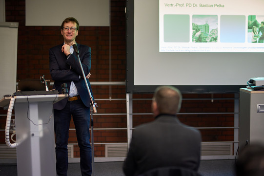 Foto. Vertr.-Prof. PD Dr. Bastian Pelka steht vor einem Mikrofon.