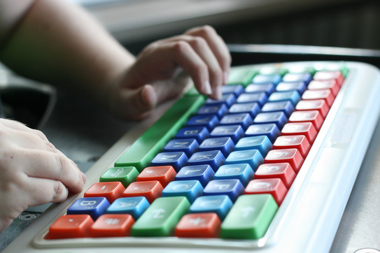 Foto. Eine Nahaufnahme von Händen, die auf einer bunten Tastatur tippen.