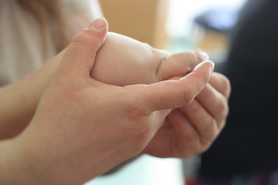 Foto. Zwei Hände, die sich um das Handgelenk einer dritten Hand legen.