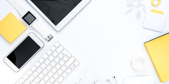 In weiß und gelb gehaltene Gegenstände für die Organisation: Tablet. Büroklammern, Schere, Smartphone, Notizblock, Uhr, Tastatur, Post-It, Thesafilm, Lineal. 